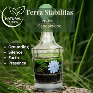 Può includere: Una bottiglia in vetro trasparente con tappo sferico, decorata con un fiore azzurro e foglie verdi dipinti a mano. Il testo riporta: Terra Stabilitas, Vetiver + Sandalwood, 100% NATURAL, Grounding, Silence, Earth, e Presence.