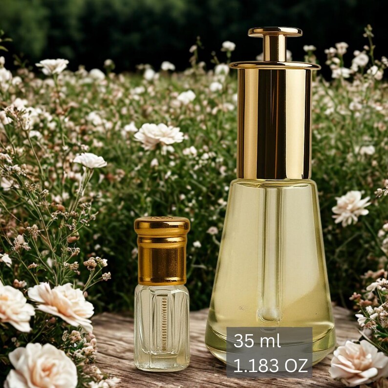 Puede incluir: Dos frascos de perfume de vidrio con tapas y detalles dorados. El frasco m&aacute;s grande est&aacute; lleno de un l&iacute;quido amarillo claro y tiene una tapa dorada. El frasco m&aacute;s peque&ntilde;o tambi&eacute;n est&aacute; lleno de un l&iacute;quido amarillo claro. El texto de la imagen dice "35 ml 1.183 OZ".