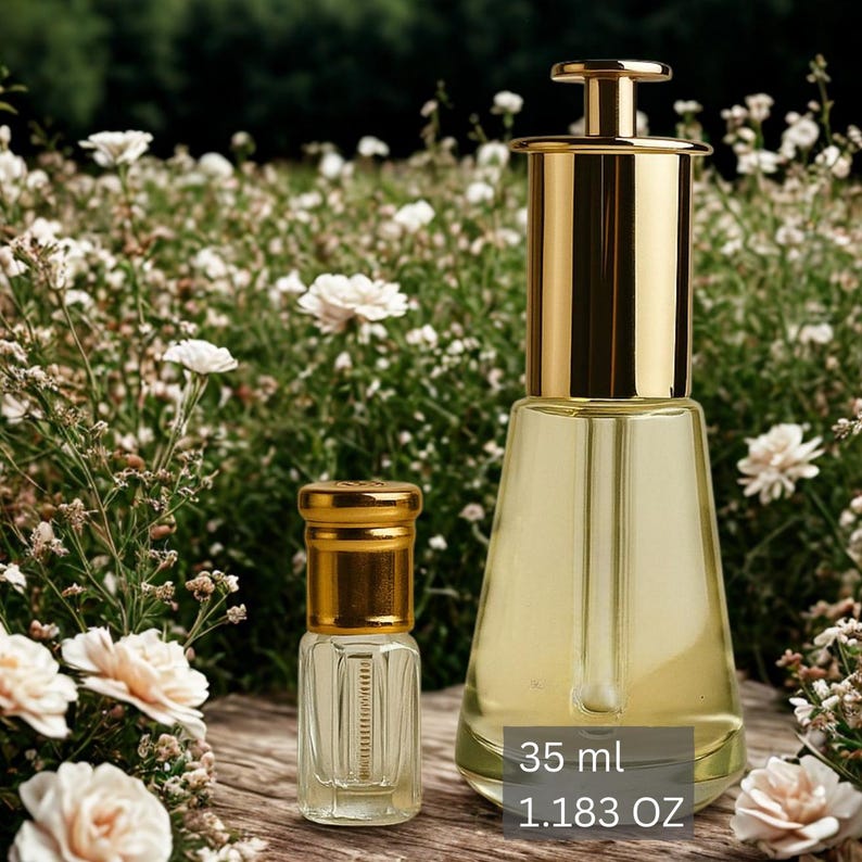 May include: Two glass perfume bottles with gold-colored caps and accents. The larger bottle is filled with a light yellow liquid and has a gold-colored top. The smaller bottle is also filled with a light yellow liquid. The text on the image reads "35 ml 1.183 OZ".