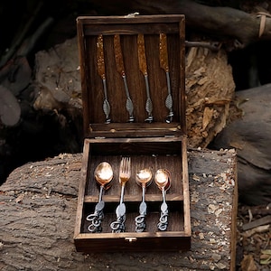 May include: A wooden box set containing a complete flatware set. The set includes four knives with textured gold blades and four spoons, a fork, and two spoons with copper-colored bowls. The handles feature a leaf design.