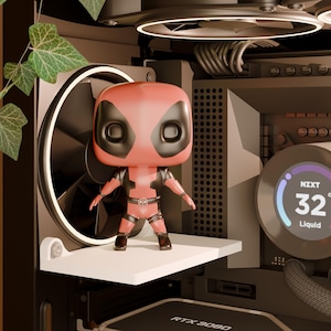 May include: A Deadpool Funko Pop figure stands on a white shelf inside a computer case. The case has a black fan and the NZXT logo. The temperature display reads 32 degrees. Green leaves hang from above.