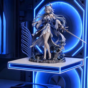 May include: A detailed anime-style figurine of a character with long silver hair, wearing a blue and white dress with flowing sleeves. The figure holds a slender sword in one hand and stands on a rocky base decorated with small blue flowers.