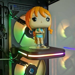 Op de afbeelding: Een Funko Pop-figuur van een personage met oranje haar en een blauwe outfit, staand op een plank in een computerkast. De kast heeft kleurrijke LED-verlichting en ventilatoren.