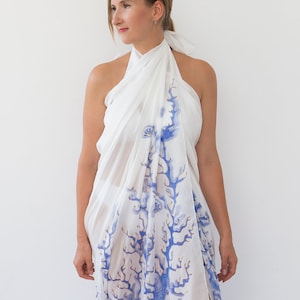 Könnte beinhalten: Ein weißer Sarong mit einem blauen und goldenen Korallenmuster. Der Sarong ist um die Schultern einer Person gelegt und am Hals gebunden.