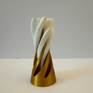 May include: A white ceramic vase with a gold base. The vase is twisted and has a unique design.