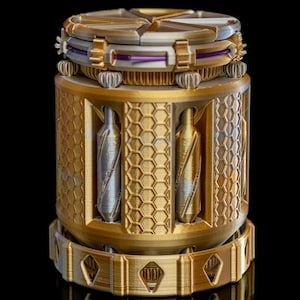 Puede incluir: Objeto cilíndrico multicapa con una combinación de colores dorados y plateados. El diseño incorpora patrones geométricos, incluyendo formas de panal y diamante. La parte superior presenta un diseño segmentado con acentos morados, y los lados tienen elementos verticales en forma de botella.