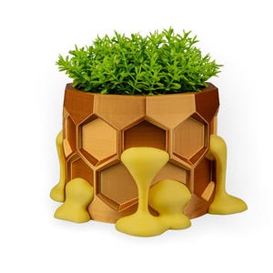 May include: A unique, geometric planter with a honeycomb design in shades of brown. The planter features yellow, drippy accents and is filled with vibrant green foliage. This decorative piece is ideal for adding a touch of modern flair to any space.