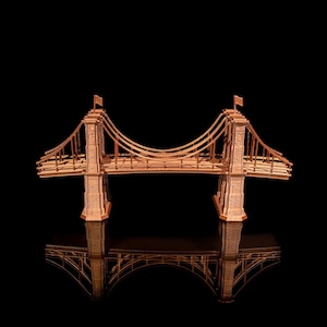 May include: A wooden model of a suspension bridge with a brown finish. The bridge is reflected in a black surface, creating a symmetrical image.