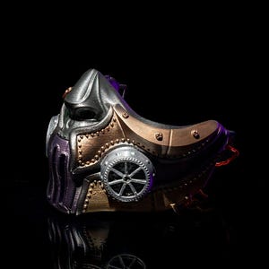 May include: A steampunk-style mask in metallic silver, bronze, and purple. The mask features intricate details, including a gear-shaped element and rivet accents. The design has a futuristic, industrial aesthetic.