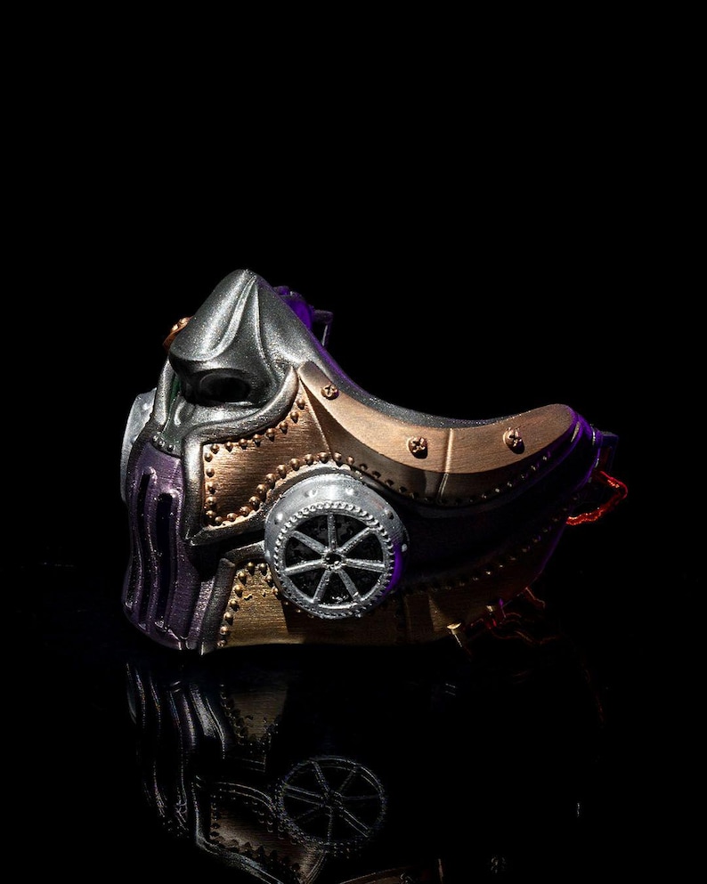 May include: A steampunk-style mask in metallic silver, bronze, and purple. The mask features intricate details, including a gear-shaped element and rivet accents. The design has a futuristic, industrial aesthetic.