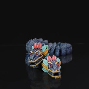 May include: Two detailed dragon head sculptures with blue, red, yellow, and green accents. The dragon heads are facing forward, with intricate details on the face and head. The background is black, and the sculptures are reflected on the surface.