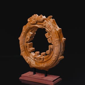 May include: A detailed, brown, circular sculpture of a dragon eating its tail, mounted on a red rectangular base. The sculpture has an open center and is supported by two black metal rods. The dragon's head is at the top of the circle.