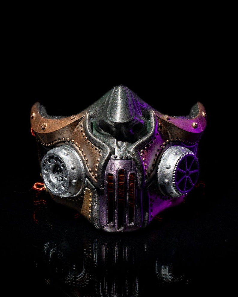 May include: A steampunk-style mask with a metallic finish. The mask features a central nose piece, two circular side vents, and a series of rivets. The color palette includes silver, bronze, and purple accents, creating a futuristic aesthetic.