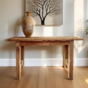 Puede incluir: Una mesa de madera rústica con un acabado marrón natural. La mesa tiene un diseño sencillo con dos patas a cada lado y una tapa rectangular. La mesa está hecha de madera recuperada y tiene un aspecto desgastado.