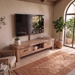 Puede incluir: Un salón con un mueble de TV de madera marrón claro, con dos cajones y un borde natural. Un televisor de pantalla plana grande está montado encima del mueble. La habitación incluye una alfombra tejida, una planta en maceta y un sillón beige.