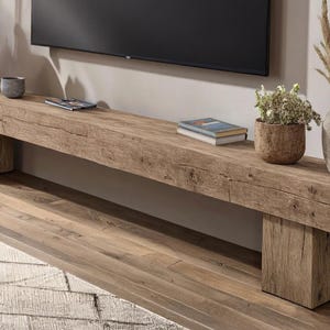May include: A long, rectangular media console crafted from reclaimed light brown wood with a visible grain and natural cracks. The console is supported by two thick, block-style legs on either end, featuring a rough, textured surface finish.