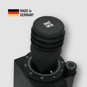 Puede incluir: Un molinillo de café negro con un dial y una tapa con el texto "md ura". El molinillo tiene una etiqueta "Made in Germany" con la bandera alemana. El dial tiene números del 0 al 90.