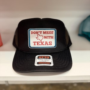 Può includere: Cappellino da camionista nero con una toppa bianca che dice "Don't Mess With Texas" in lettere rosse e blu. La toppa presenta un contorno bianco dello stato del Texas. Il cappello ha anche un'etichetta nera che dice "Otto World Famous Foam Front Trucker".