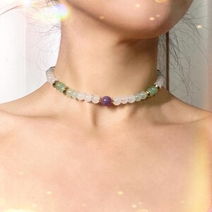May include: A delicate choker necklace with light green and white beads, accented by a single purple bead in the center.