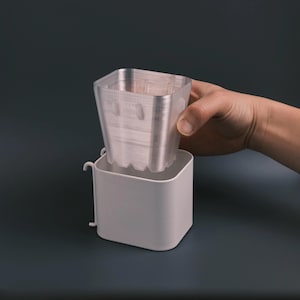 May include: A white plastic planter with a clear plastic insert. The insert is being lifted out of the planter.