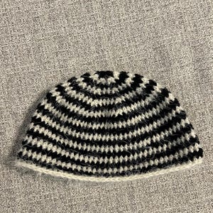 May include: A handmade crochet beanie hat with a black and white striped pattern. The hat is made of soft yarn and has a white brim. The hat is designed to fit snugly on the head and is suitable for cold weather.