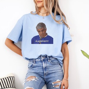 May include: A light blue t-shirt with a graphic of a man with a microphone saying "PLAYOFFS??" in white text.