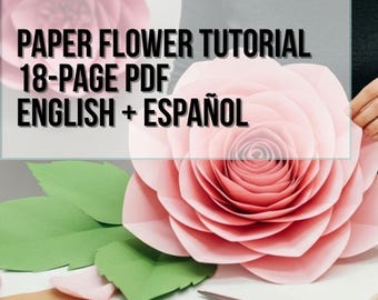May include: A large, light pink paper flower with layered petals and green paper leaves. The image includes text that reads: PAPER FLOWER TUTORIAL 18-PAGE PDF ENGLISH + ESPAÑOL. A pair of black and orange scissors rests on the surface nearby.