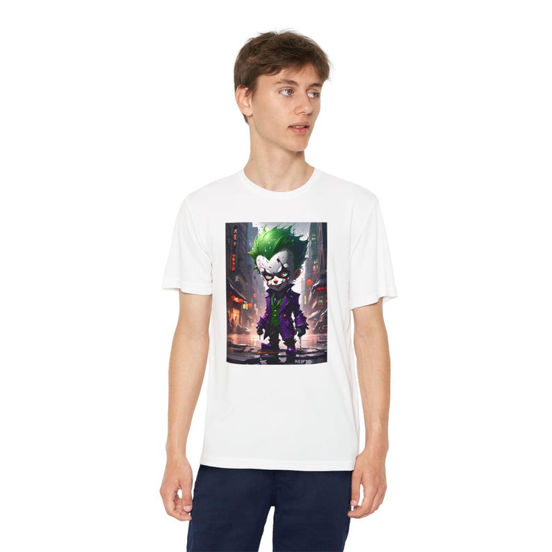 May include: White t-shirt featuring a graphic print of a cartoon Joker character in a purple suit and green hair. The Joker is standing in a dark city alley.