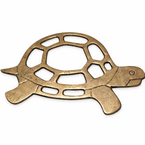 May include: A bronze-colored turtle-shaped decorative item. The turtle has a detailed shell with open geometric shapes and is lying on a white background. The turtle's head and legs are solid.