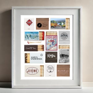 May include: A framed collage of matchbox labels featuring various ski resorts and businesses in Aspen, Colorado. The labels are arranged in a grid pattern and include names like "Ajax", "The Little Nell", "Highland Bowl", "White House Tavern", "Casa Tua", "Aspen Snowmass", "Kemo Sabe", "Meat & Cheese", "Jerome", and "Paradise".