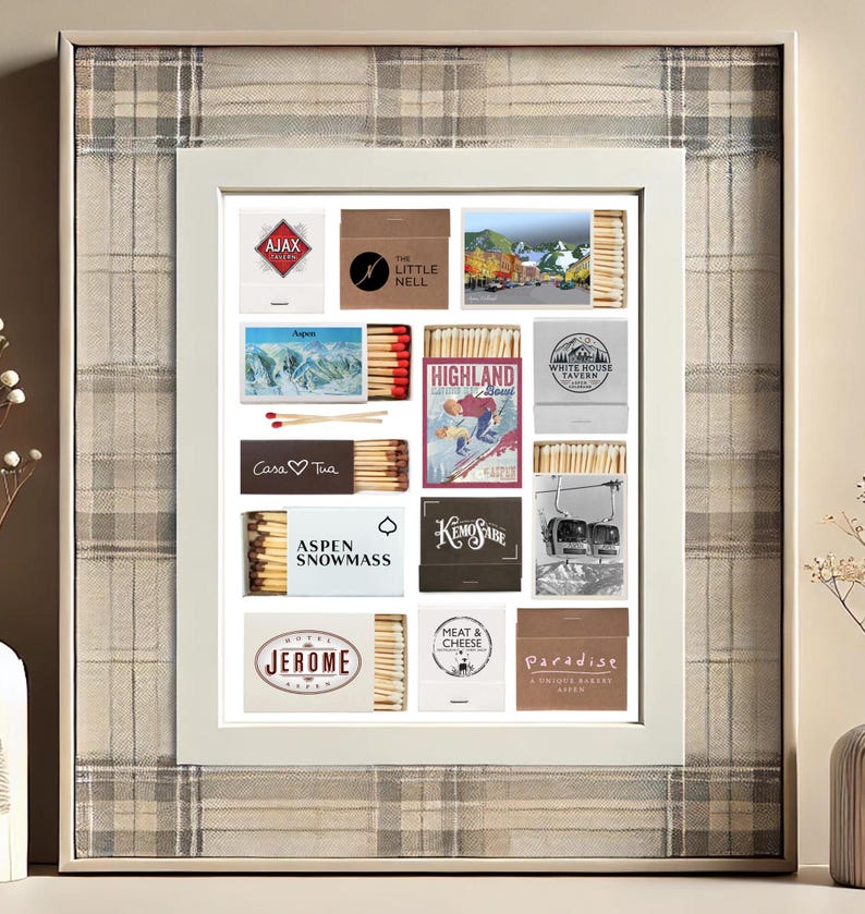 May include: A white frame with a collage of matchbox labels. The labels feature various designs, including mountains, ski resorts, and cityscapes. The labels are arranged in a grid pattern and are surrounded by a white border.