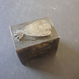 Può includere: Un blocco di stampa in legno vintage con un motivo a cuore intagliato. Il blocco è in legno scuro e ha un aspetto usurato e invecchiato.
