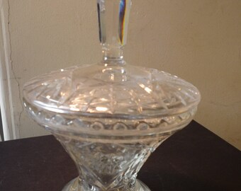 May include: A clear glass candy dish with a lid. The dish has a cut glass design and a pointed top.