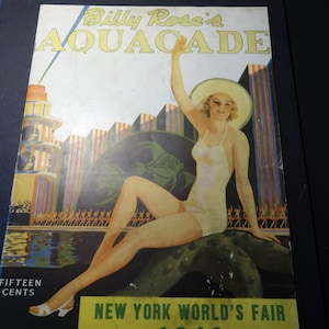 May include: A vintage poster advertising Billy Rose's Aquacade at the 1939 New York World's Fair. The poster features a woman in a white swimsuit and a large hat, sitting on a rock in front of a colorful backdrop of the Aquacade stage. The text "FIFTEEN CENTS" is printed at the bottom left corner of the poster.