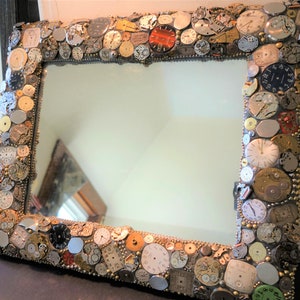 Puede incluir: Un espejo rectangular con un marco hecho de cientos de pequeñas piezas de reloj redondas y plateadas. El marco es un mosaico de esferas de reloj, engranajes y otras piezas de reloj.