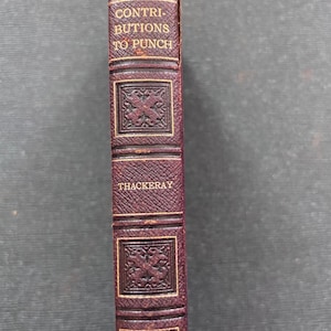 Pode incluir: Um livro encadernado em couro bordô com letras douradas. O título é "Contributions to Punch" de Thackeray. O livro é publicado por Oxford.