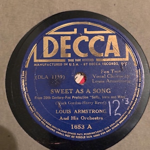 May include: A blue and gold vinyl record with the label "Decca" and the title "Sweet As A Song" by Louis Armstrong and His Orchestra. The record number is 1653 A.