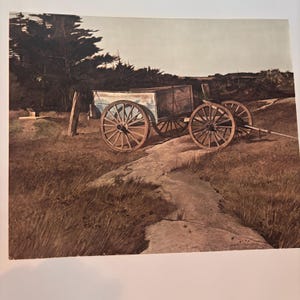 May include: A vintage wooden cart with large spoked wheels stands on a dirt track. The cart's body is painted light blue. The scene is a landscape with brown grass, trees, and a pale sky. A wooden fence post is in the foreground.