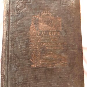 May include: A weathered brown hardcover book with an embossed cover featuring decorative corner scrollwork. The center displays a faint illustration of a flag and the text Life with the 10th Massachusetts Volunteers, showing signs of age and wear.