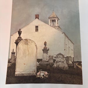May include: A painting of a white church with a steeple in a graveyard. The image shows weathered tombstones, a muted colour palette, and a sense of historical ambience. A bouquet of flowers rests near a large tombstone.
