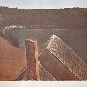 May include: A photograph of a house with a brick chimney and a wooden roof. The house is situated on a hill overlooking a body of water. The water is calm and the sky is cloudy.
