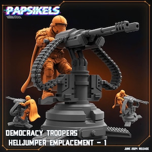 May include: A miniature orange soldier figure wearing a helmet and cape, operating a large gray mounted machine gun with ammunition belts. The text reads PAPSIKELS, DEMOCRACY TROOPERS, HELLJUMPER EMPLACEMENT - 1, and JUNE 2024 RELEASE.