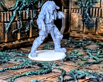 May include: A light gray Predator action figure, posed in a dynamic stance, stands on a white base. The figure is highly detailed, showcasing armor and intricate design. The background features a sci-fi themed environment with green vines.