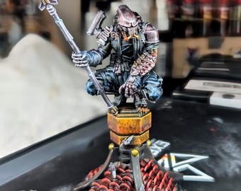 May include: A detailed miniature figure of a warrior, holding a spear. The figure is painted in shades of gray, blue, and bronze, and is posed on a decorative stand with red and gold accents. The figure is a collectible item.
