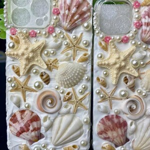 May include: A white phone case decorated with seashells, starfish, and pearls. The case has a clear back panel and a white border.