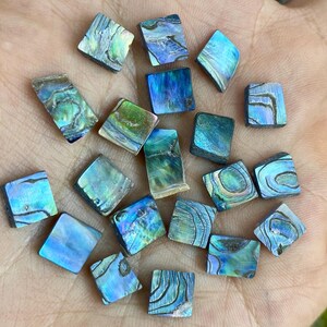May include: A collection of iridescent abalone shell squares in various shades of blue, green, and purple. The squares are approximately 1 inch in size and have a smooth, polished surface.