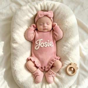 Puede incluir: Un beb&eacute; con un mameluco de manga larga de punto acanalado en color rosa empolvado, con dobladillo con volantes y el nombre Josie bordado en letra cursiva blanca en el pecho. Incluye una diadema a juego con lazo y patucos de punto suave.