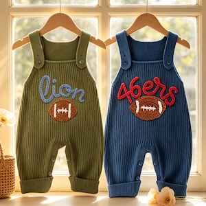 May include: Two ribbed knit rompers hanging on wooden hangers. The olive green romper features the word "lion" in blue yarn and a brown football applique. The navy blue romper features the word "46ers" in red yarn and a brown football applique.