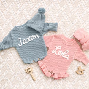 Puede incluir: Un pelele de punto azul de manga larga con el nombre Jaxon bordado en blanco, junto a un gorro con pomp&oacute;n a juego, y un pelele de punto rosa de manga larga con el nombre Lola bordado en blanco, que presenta un dobladillo con volantes.