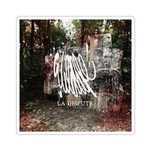 May include: Square sticker featuring a graffiti-covered concrete structure in a forest setting. The structure is painted with white abstract designs and the words "LA DISPUTE" in white text. The background is a blurred view of trees.